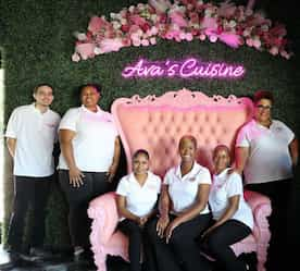 Team picture by a big pink chair and their name behind them