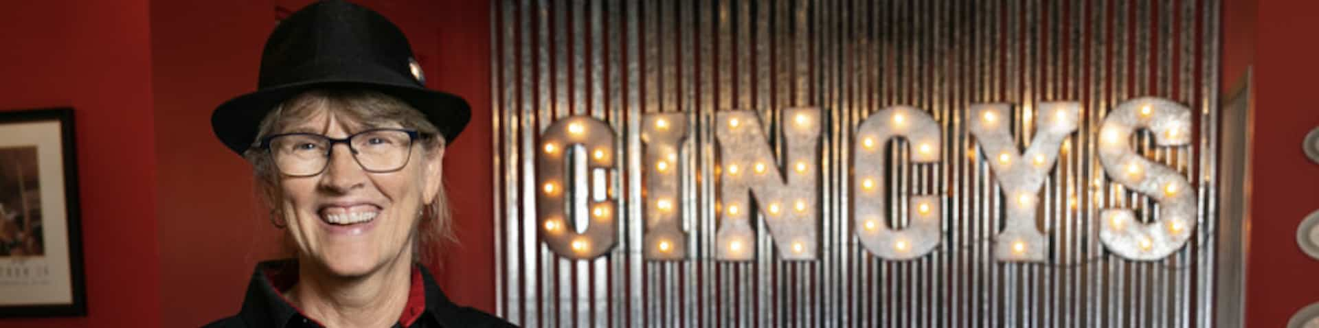 Owner in front of restaurant name lit up behind her