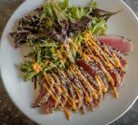 sushi with sauce drizzled over it with a salad on the side